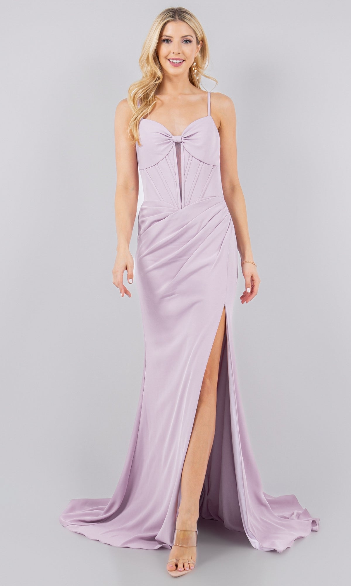 A woman wears the Pleated Corset Prom Dress: Cinderella Couture 8090J, a light lavender, floor-length gown with a sweetheart neckline, spaghetti straps, fitted bodice, and front slit, standing against a plain gray background.